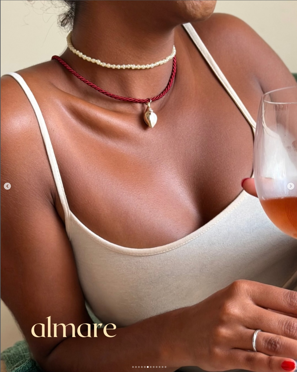 Close de colares almare com cordão vinho e taça rosé em cena editorial