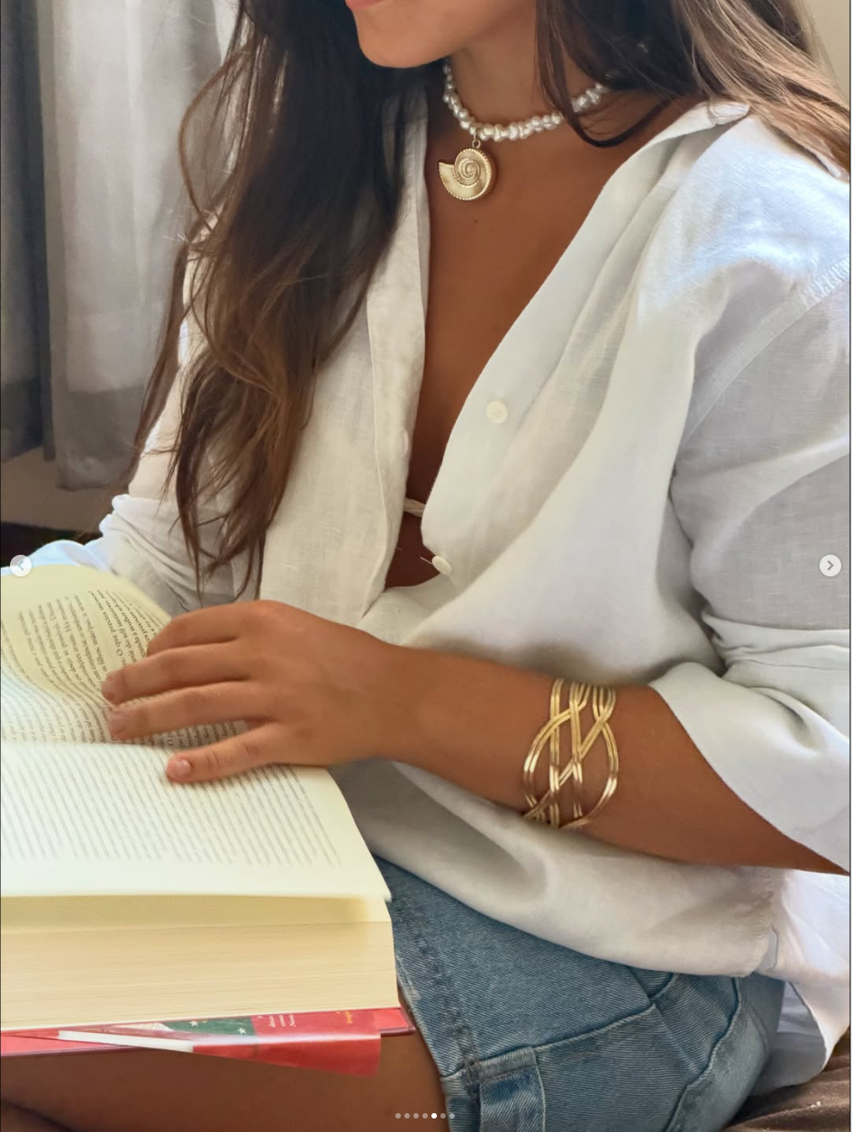 Mulher lendo com colar de pérolas almare e bracelete dourado