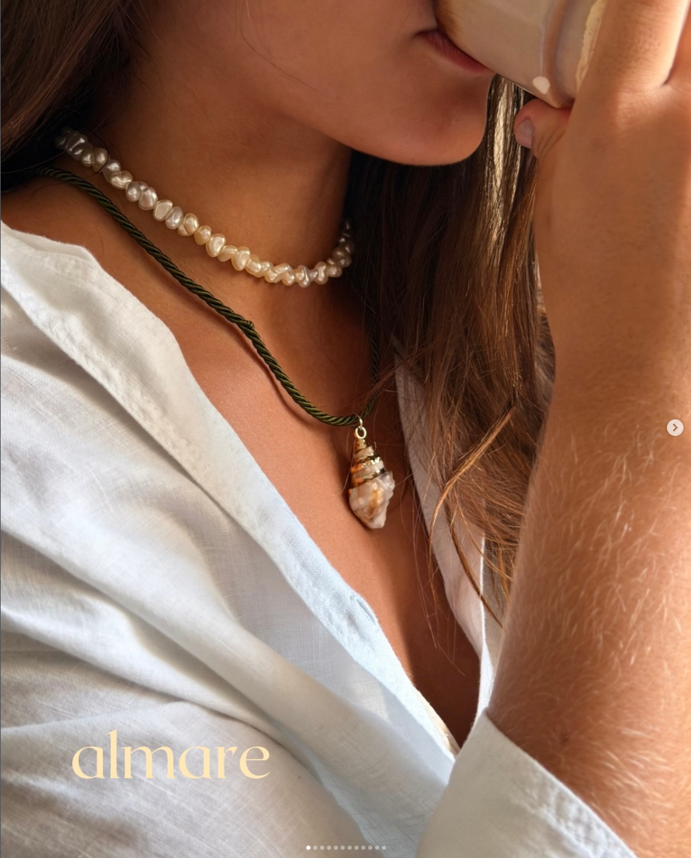 Mulher usando colares almare enquanto segura uma xícara em look de linho branco