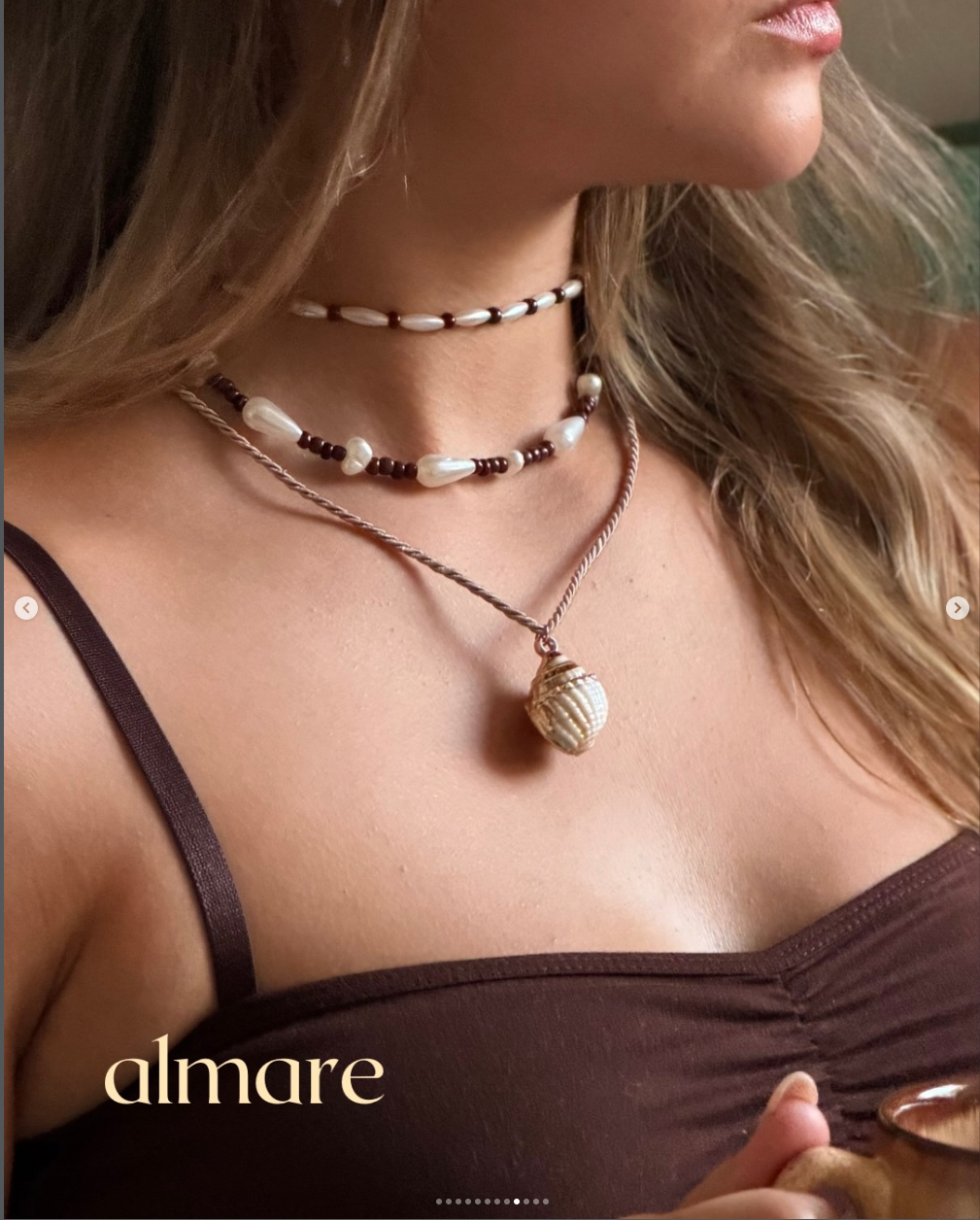Close de colar almare com pingente de concha branca em close sobre vestido marrom