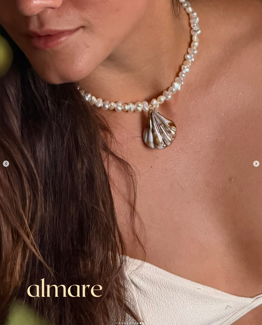 Close de colar almare com pérolas e pingente de concha sobre pele e linho claro
