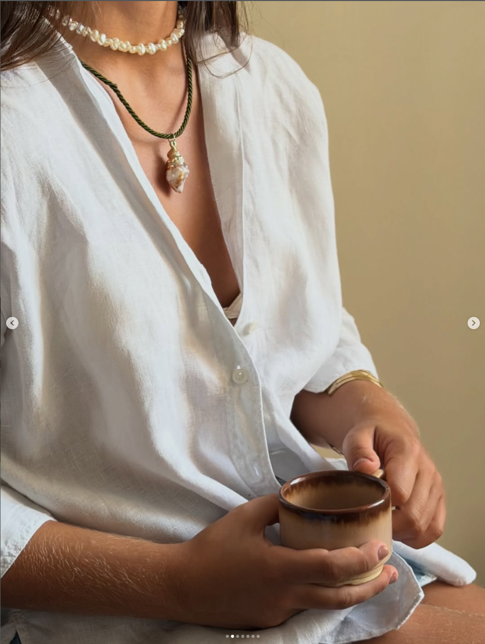 Close editorial de joia almare com pingente de concha sobre camisa branca